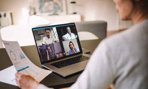 Office colleagues having a video call to discuss few financial reports. Business people working from home having a video conference. Over the shoulder view.